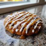 Close-up of a Crumbl caramel apple cookie with white icing and caramel drizzle.