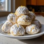 A pile of soft, round Lemon Meltaways dusted with powdered sugar and topped with bright yellow lemon zest.