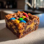 A close-up of a monster cookie brownie topped with colorful M&Ms and chocolate chips.