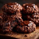 Close-up of rich chocolate no bake keto cookies, one broken in half, drizzled with glossy chocolate sauce.