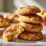 A stack of freshly baked peach snickerdoodle cookies, with one cookie broken in half to reveal juicy peach pieces inside.
