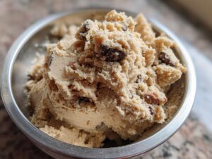 Close-up of a metal bowl filled with creamy protein cookie dough, studded with chocolate chips.