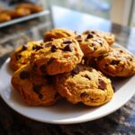 A close-up of a stack of freshly baked pumpkin chocolate chip cookies on a white plate.
